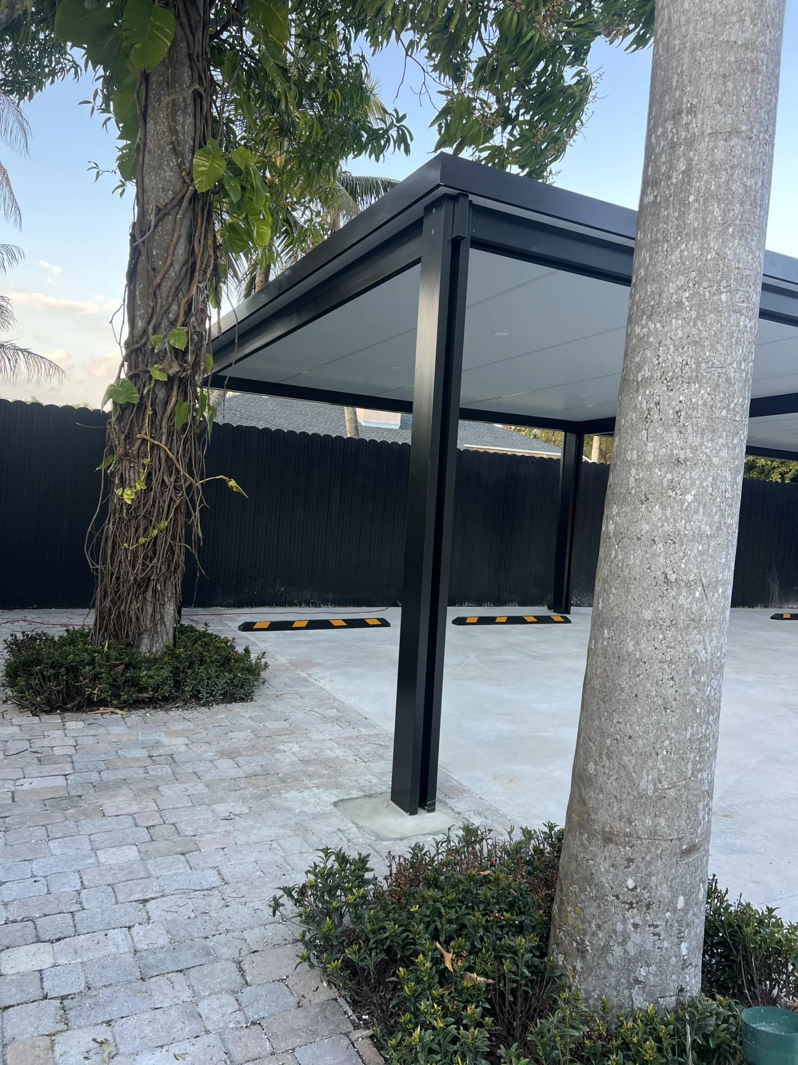Black aluminum pergola carport over a paved driveway